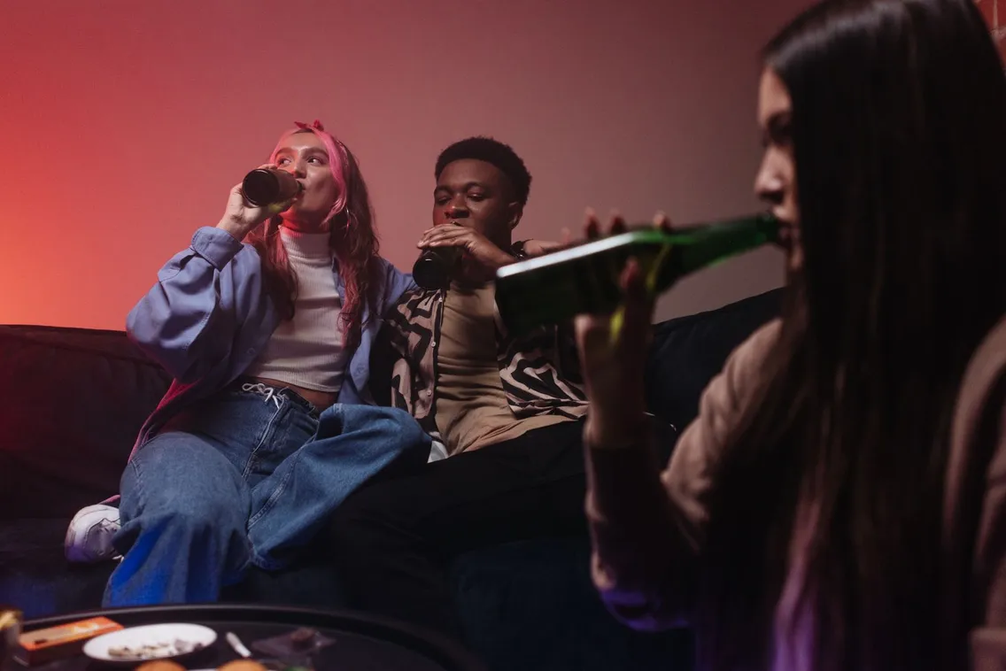 Eine Gruppe von Freunden trinkt bei einer Party in einer Wohnung Bier auf dem Sofa
