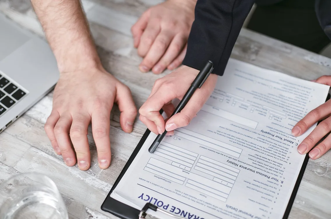 Two people signing an insurance policy on a wooden table