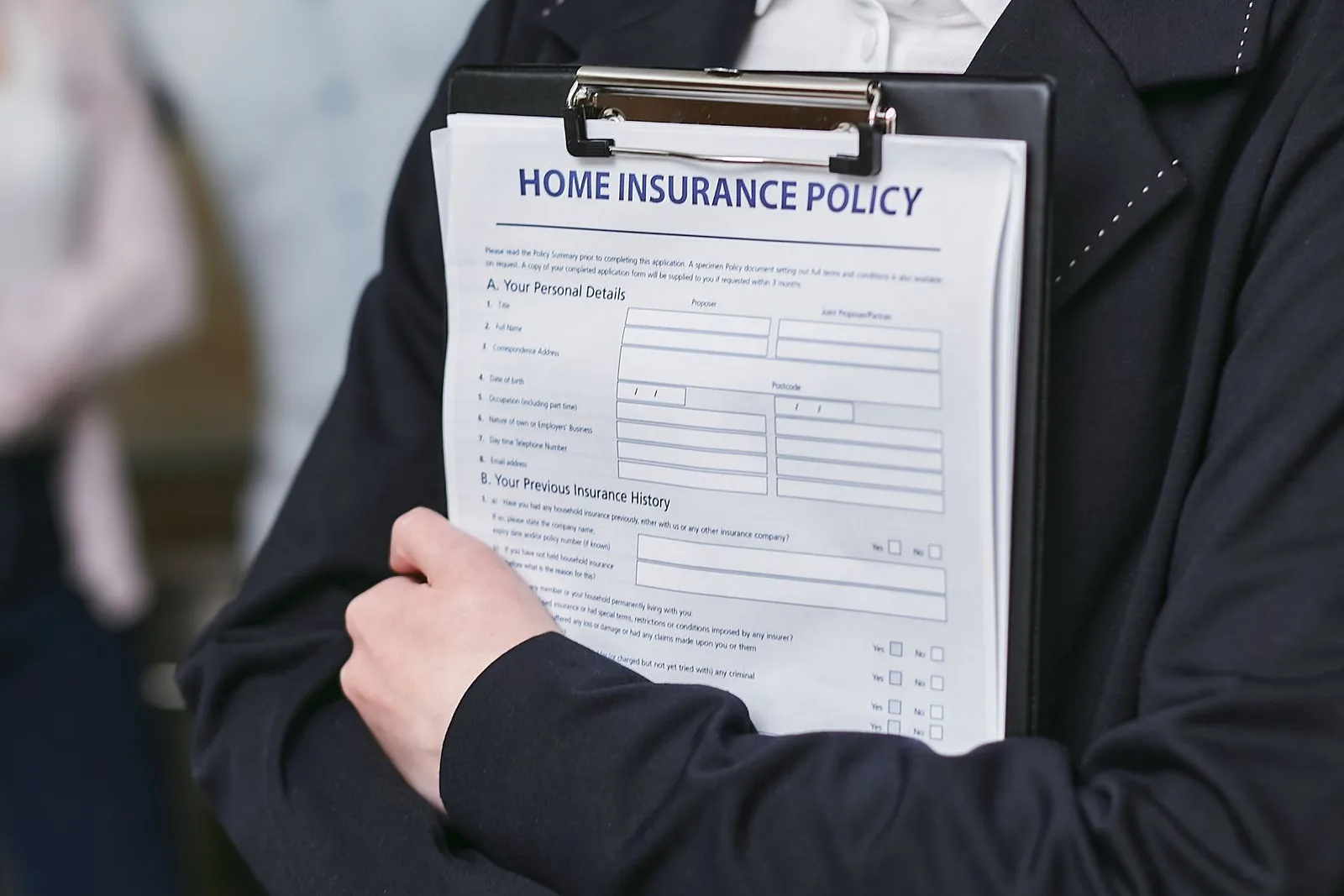 A person in a blazer holding a clipboard with a home insurance policy
