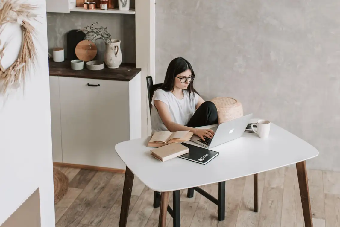 A woman writing a rental advert on a laptop at a table in a flat