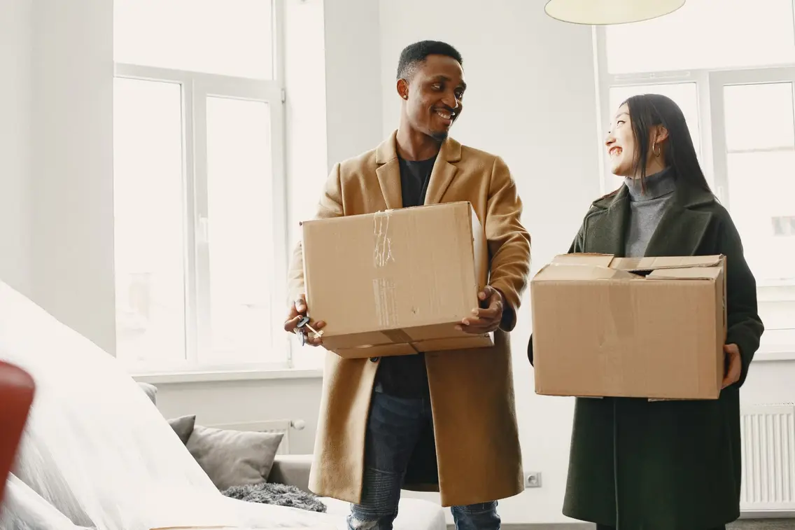 Zwei Personen tragen Umzugskartons in eine neu gemietete Wohnung