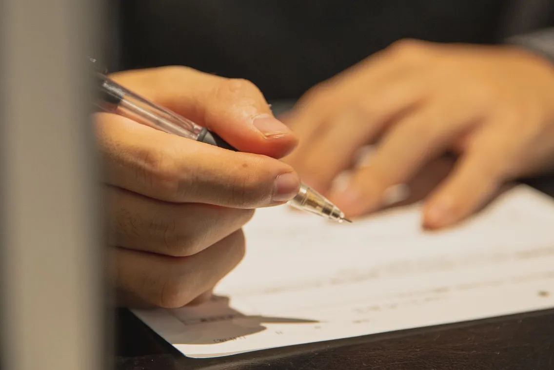 Eine Hand mit Stift füllt ein Papierformular auf einem Tisch aus