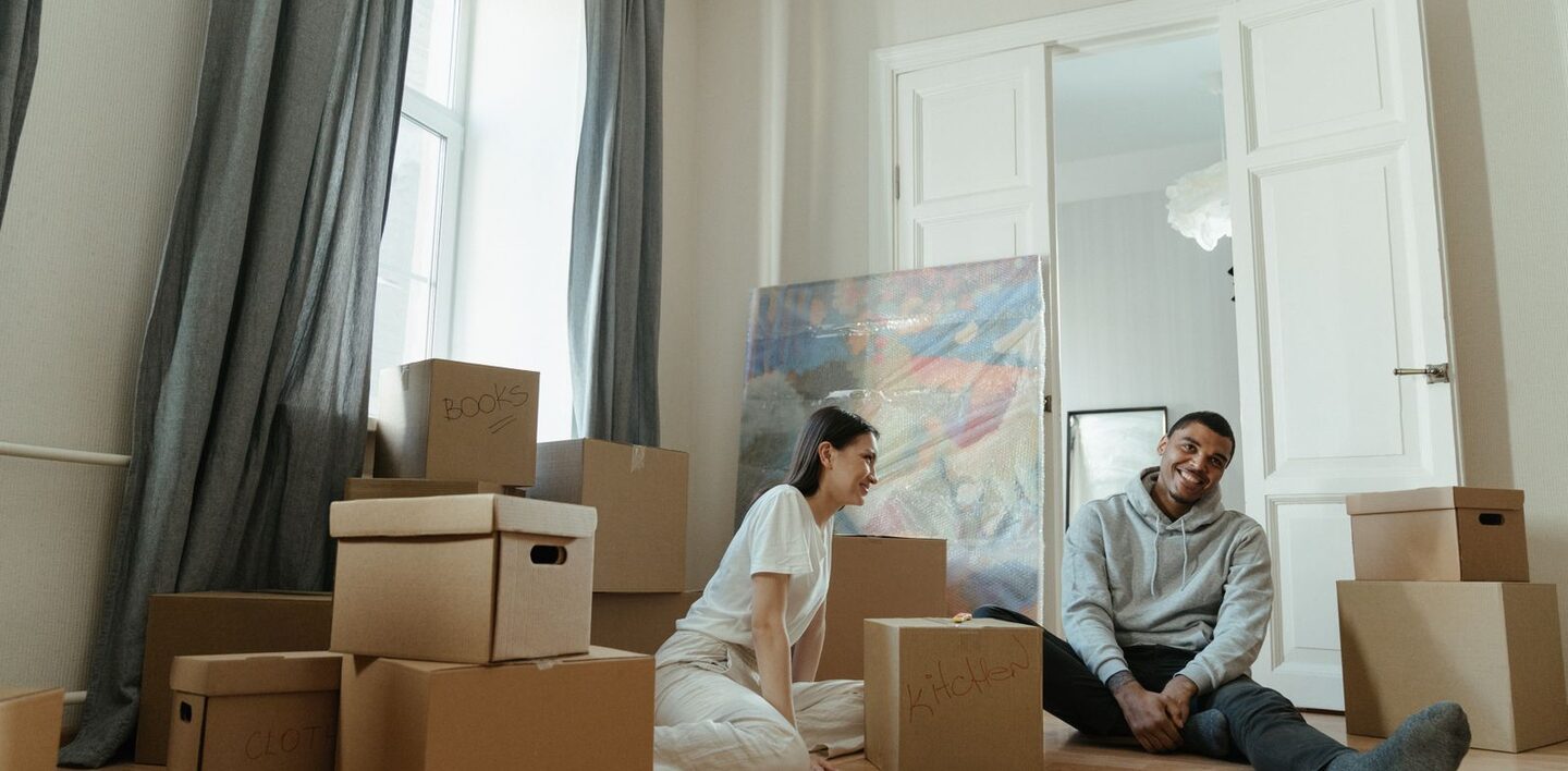 Ein junges Paar sitzt zwischen Umzugskartons auf dem Boden einer neuen Wohnung
