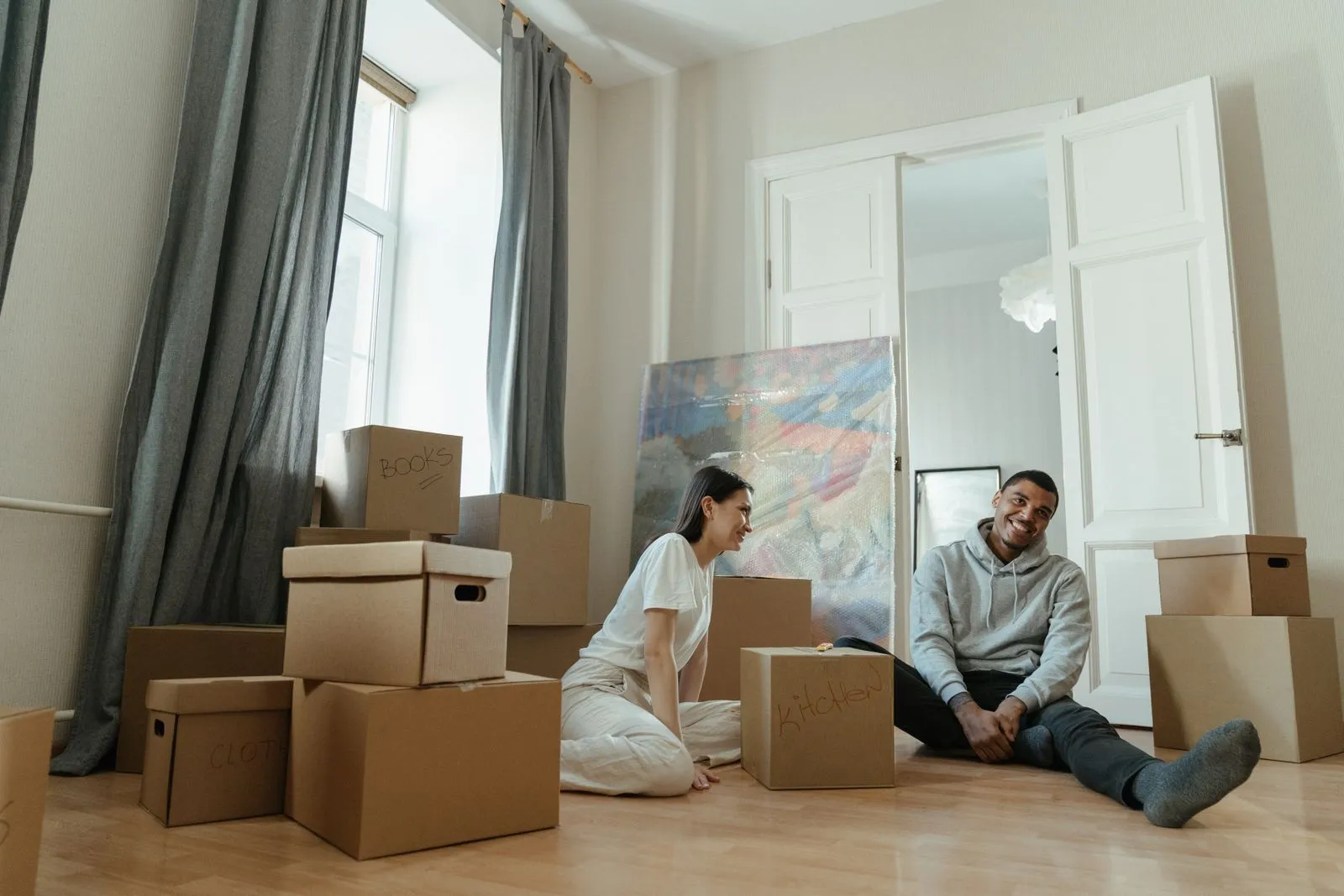 Ein junges Paar sitzt zwischen Umzugskartons auf dem Boden einer neuen Wohnung